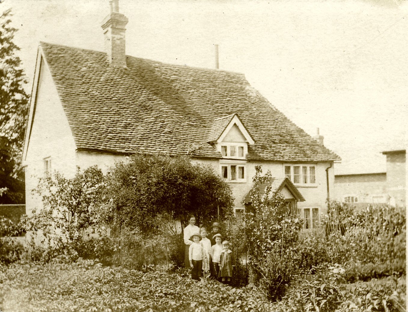 A black and white photograph of an old cottage with a woman and five children standing outside its door.