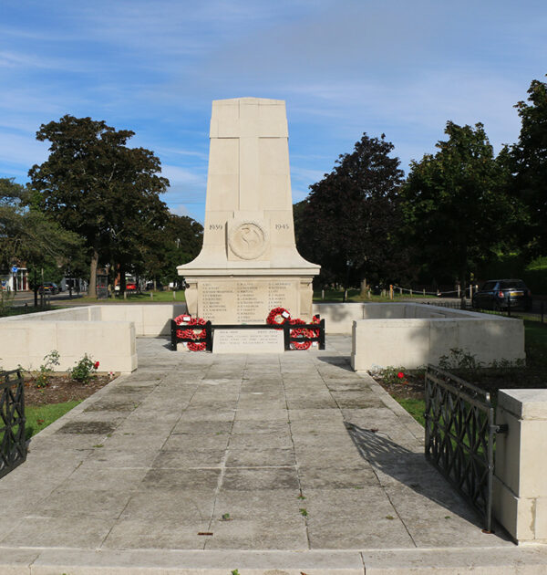 The cream war memorial in Cranleigh with red poppy wreaths laid against it